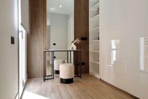 Ein modernes Interieur mit Holzboden, Glastür, Tisch mit schwarzem Rahmen und weißer Vase mit Trockenpflanzen.