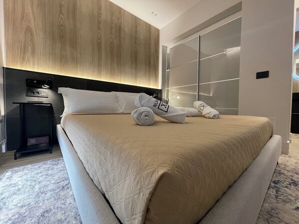 A modern hotel room with a large bed, a bedside table with a lamp, and a wardrobe with sliding doors. - Garibaldi Suites 4 · Renovated 1BR Ground-Floor Suite in Olbia Historic Centre (Olbia)