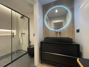 A modern bathroom with a glass shower enclosure, a black vanity with a mirror, and a wooden wall panel. - Garibaldi Suites 4 · Renovated 1BR Ground-Floor Suite in Olbia Historic Centre (Olbia)