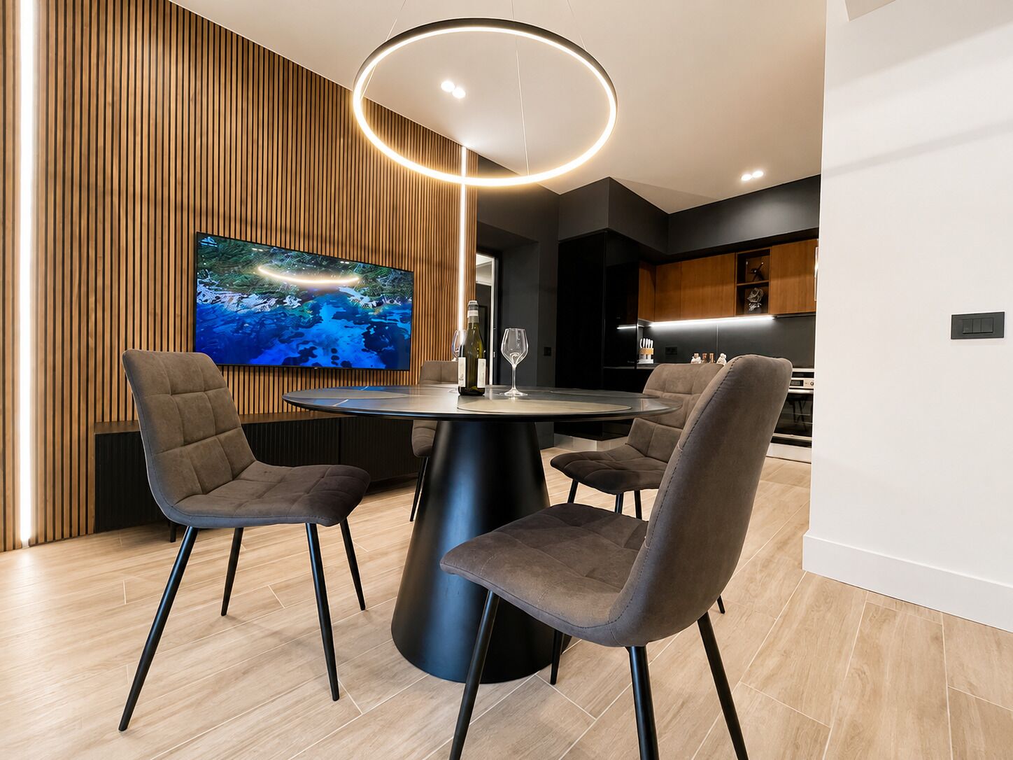 Een moderne eetruimte met een ronde tafel, vier stoelen, een grote flatscreen televisie en een opvallende, ronde lamp.