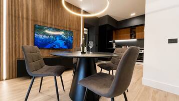 Een moderne eetruimte met een ronde tafel, vier stoelen, een grote flatscreen televisie en een opvallende, ronde lamp.