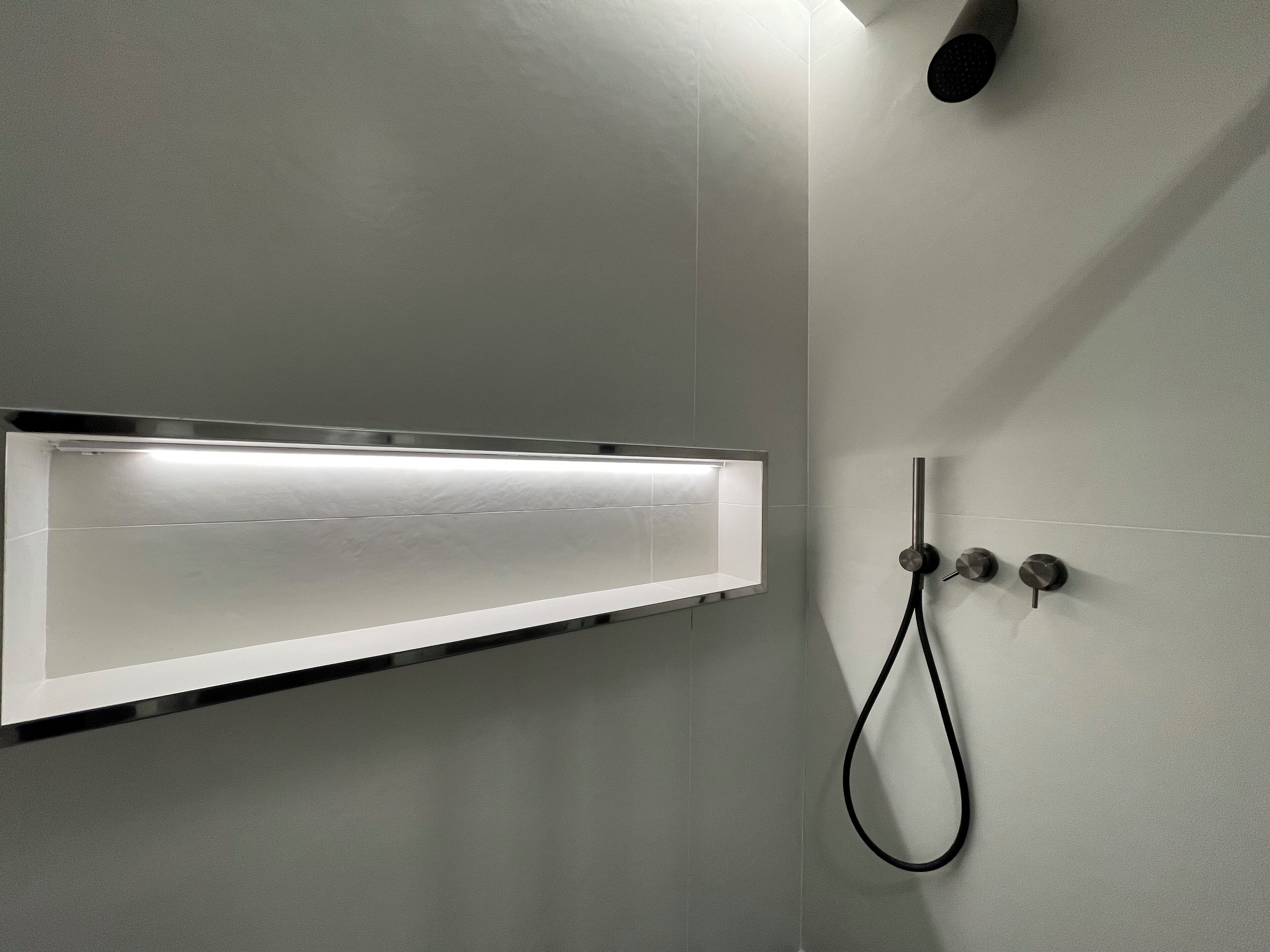 A modern shower enclosure with a wall-mounted control panel and a handheld showerhead.