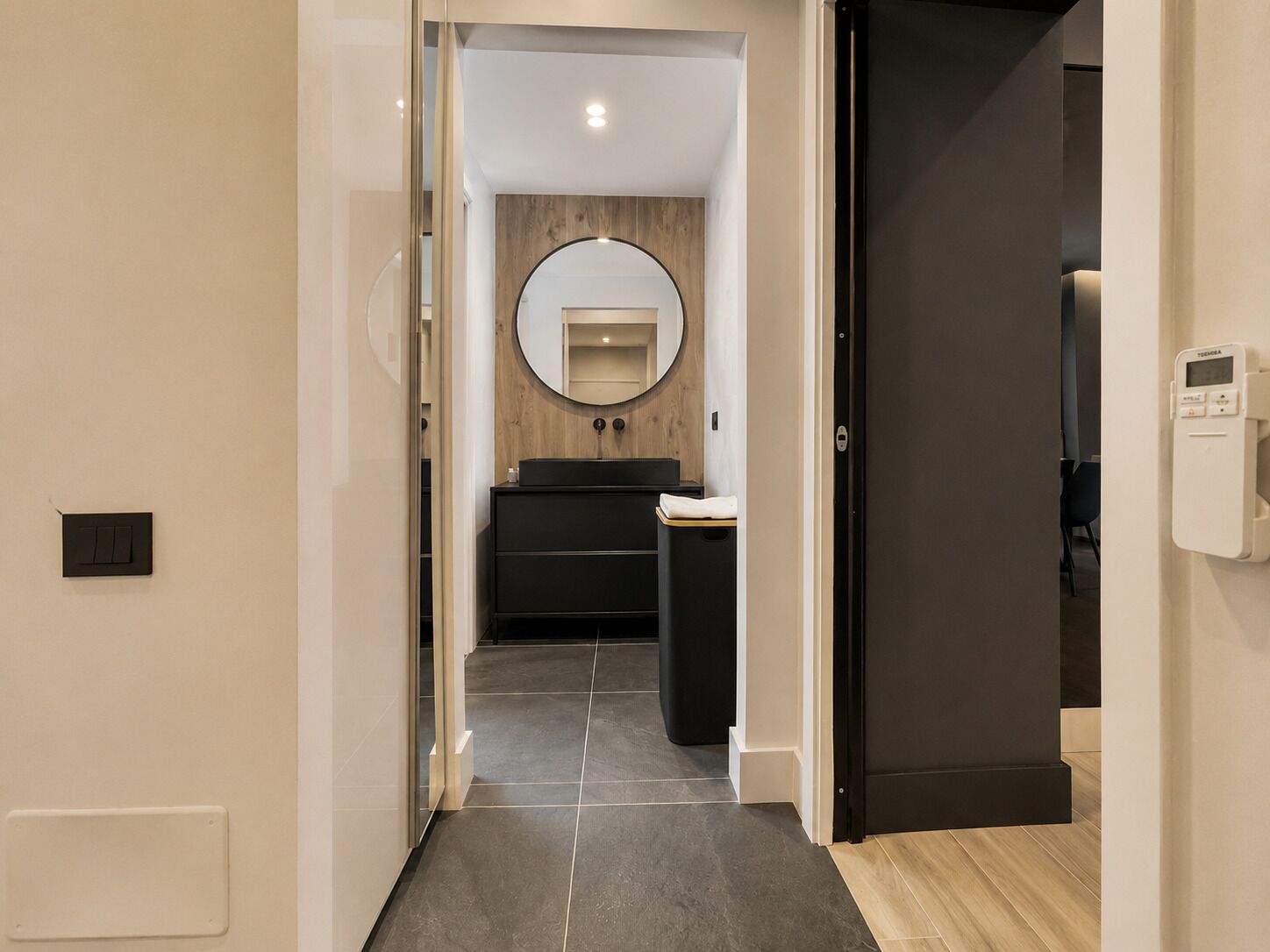 A modern bathroom with a round mirror, black vanity, and a toilet.