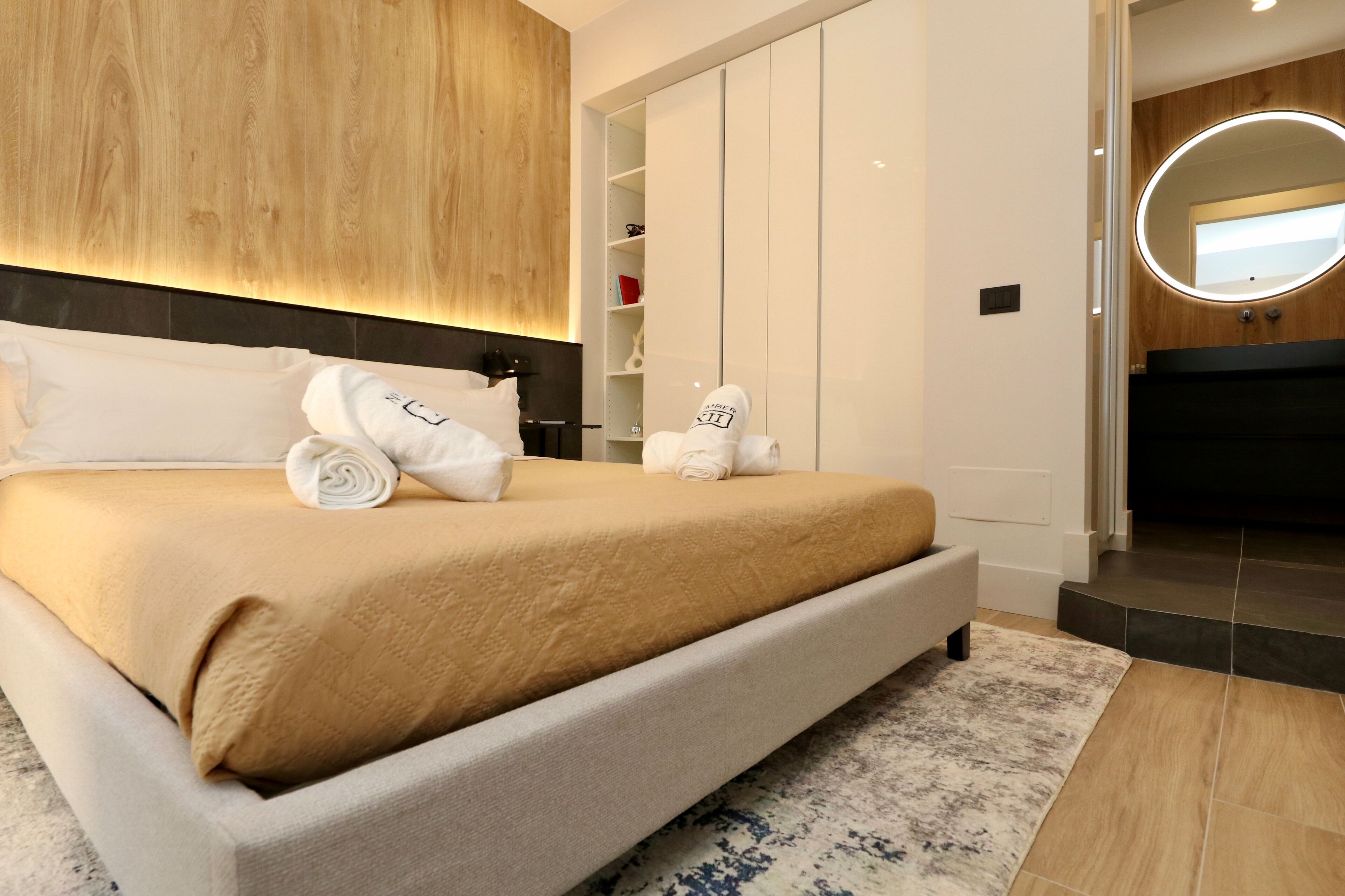 Een moderne slaapkamer met een groot bed, een houten hoofdbord, een inbouwkast en een ronde spiegel boven het bed.