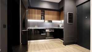 A modern kitchen with black cabinets, stainless steel appliances, and a wooden floor.