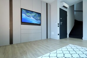 A modern living room with a flat-screen TV mounted on the wall, a staircase, and a door.