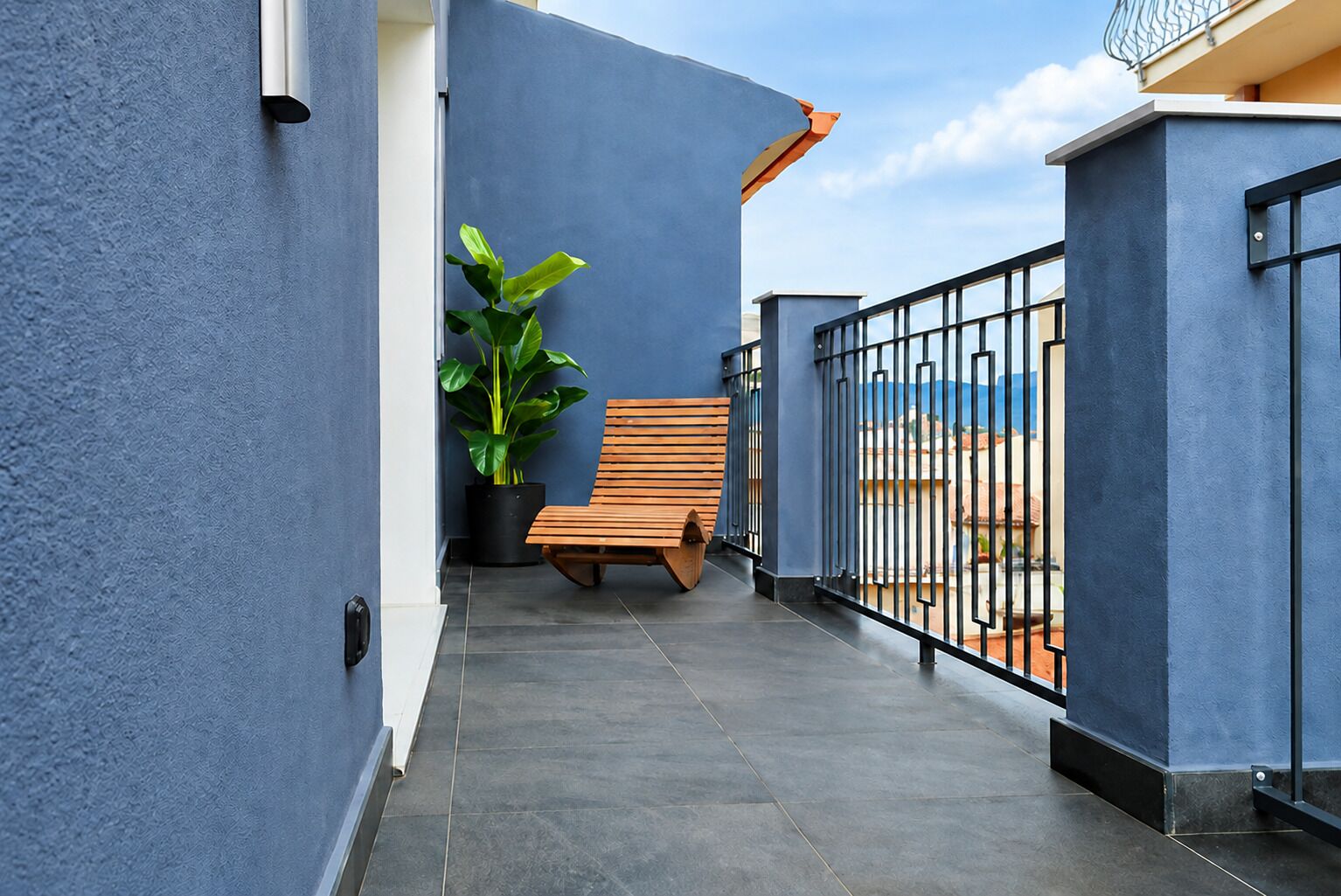 A balcony with a wooden bench, a potted plant, and a view of the sea.