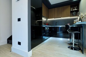 A modern kitchen with a glass partition, wooden cabinets, and a bar area with a high chair. - Garibaldi#4 - Spacious Luxury Penthouse - Private terrace w/ Seaview - Old City (Olbia)