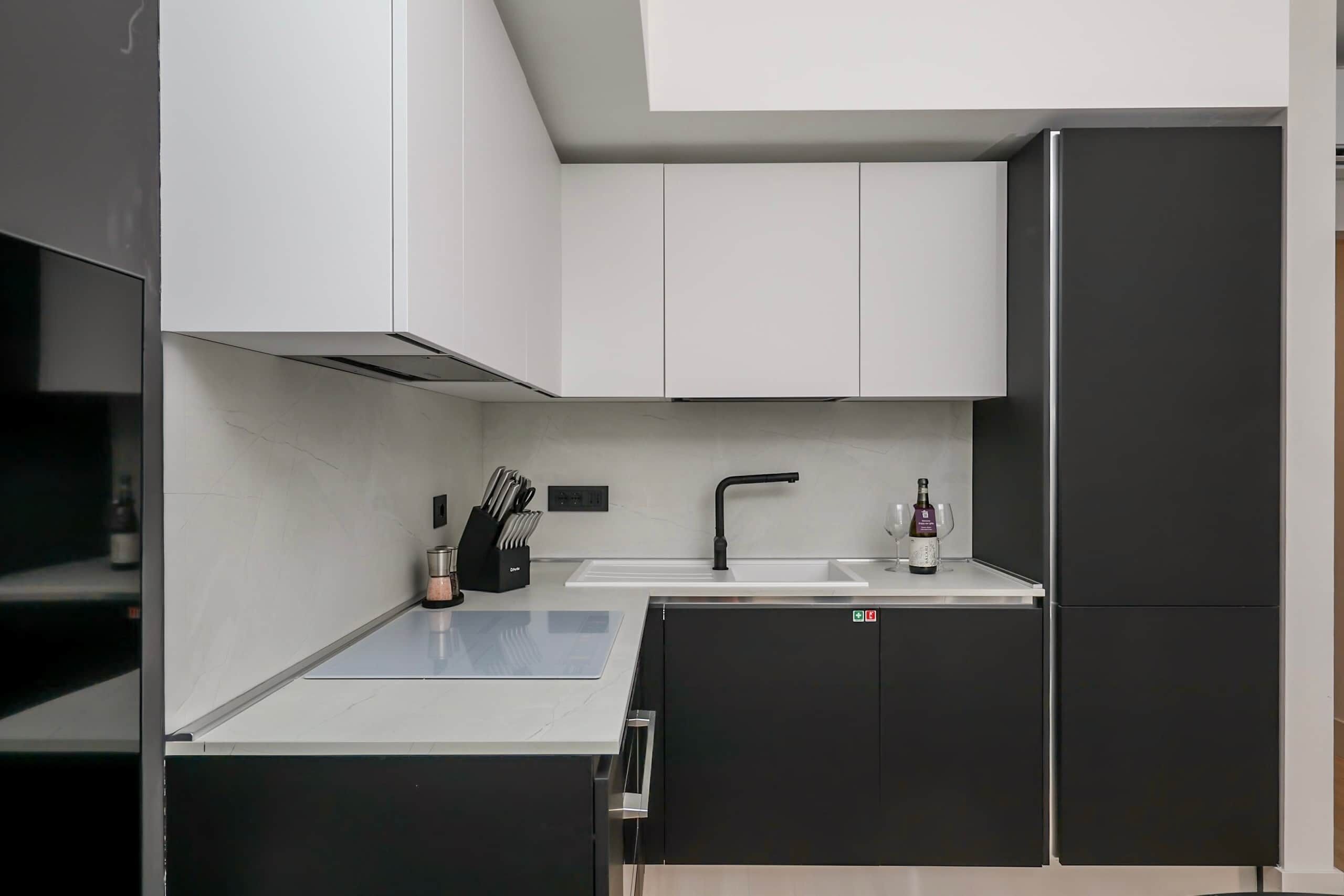 Een moderne keuken met witte kastjes, een zwarte koelkast en een ingebouwde gootsteen.