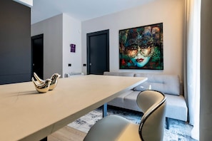 Ein modernes Wohnzimmer mit einem hellen Sofa, einem Esstisch mit zwei goldenen, vogelartigen Vasen und einem farbenfrohen abstrakten Gemälde an der Wand.