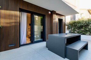 A modern outdoor seating area with a built-in bench and a table, adjacent to a sliding glass door leading into a room.
