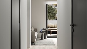 A modern hallway with a wooden floor, a sofa, a coffee table, and a view of a living area through a glass door.