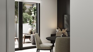 A modern interior with a dining area featuring two chairs and a table, a large window with a view of greenery, and a dark accent wall.