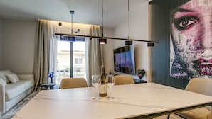 A modern living room with a large table, two wine glasses, and a bottle of wine. There is a sofa, a TV, and a large artwork on the wall. - AZULIS Apartment 7 · 2BR with Terraces & Elevator in Aldo Moro (Olbia)