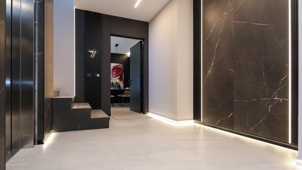A modern hallway with a marble wall, a staircase, and a door leading to a room with a red and black design. - AZULIS Apartment 7 · 2BR with Terraces & Elevator in Aldo Moro (Olbia)