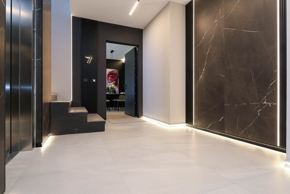 Un couloir moderne avec un mur en marbre, un escalier et une porte donnant sur une pièce au décor rouge et noir.