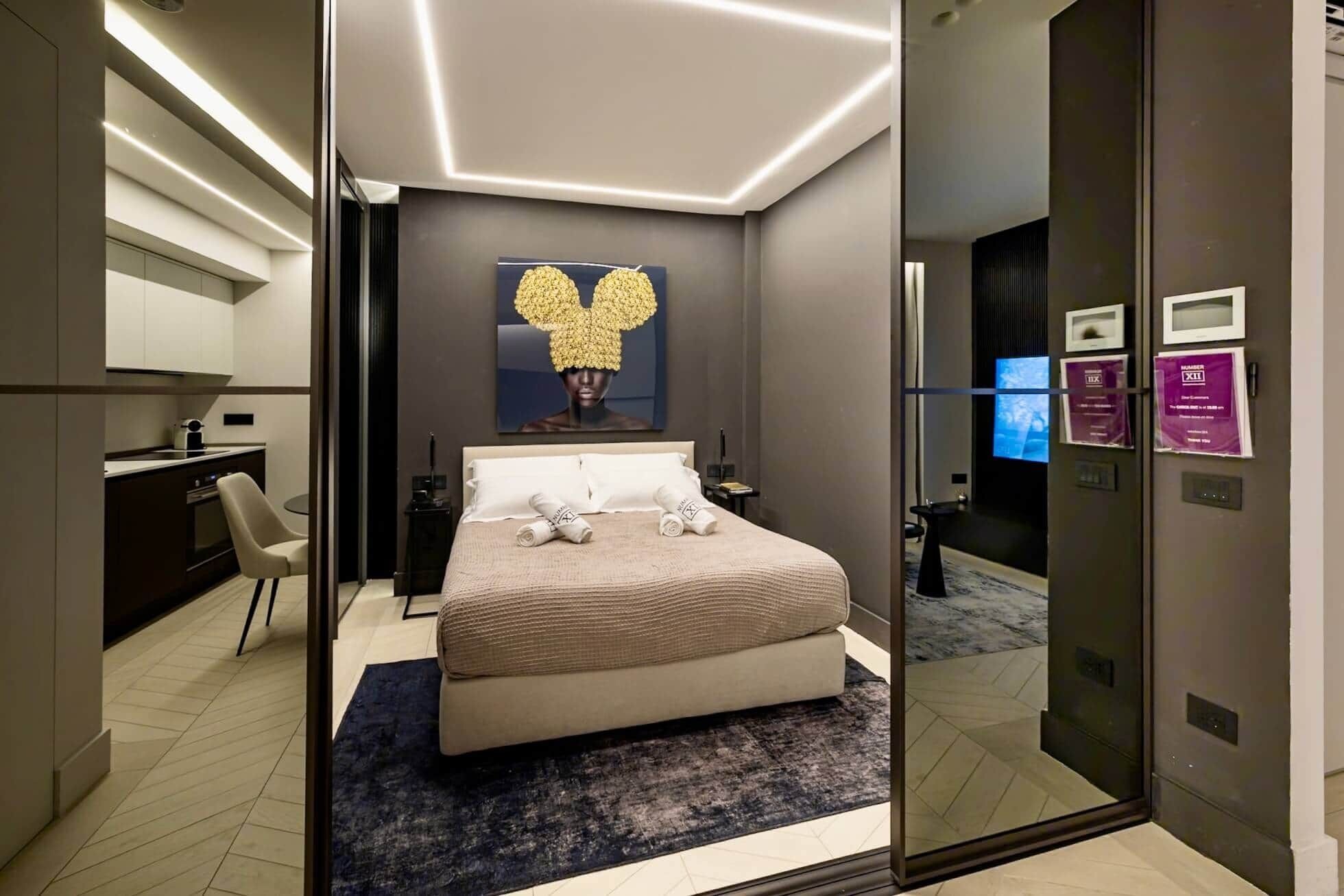 A modern hotel room with a bed, bedside table, and a large mirror.