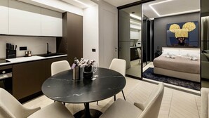 Una habitación de hotel moderna con zona de comedor, cama y ventana grande.