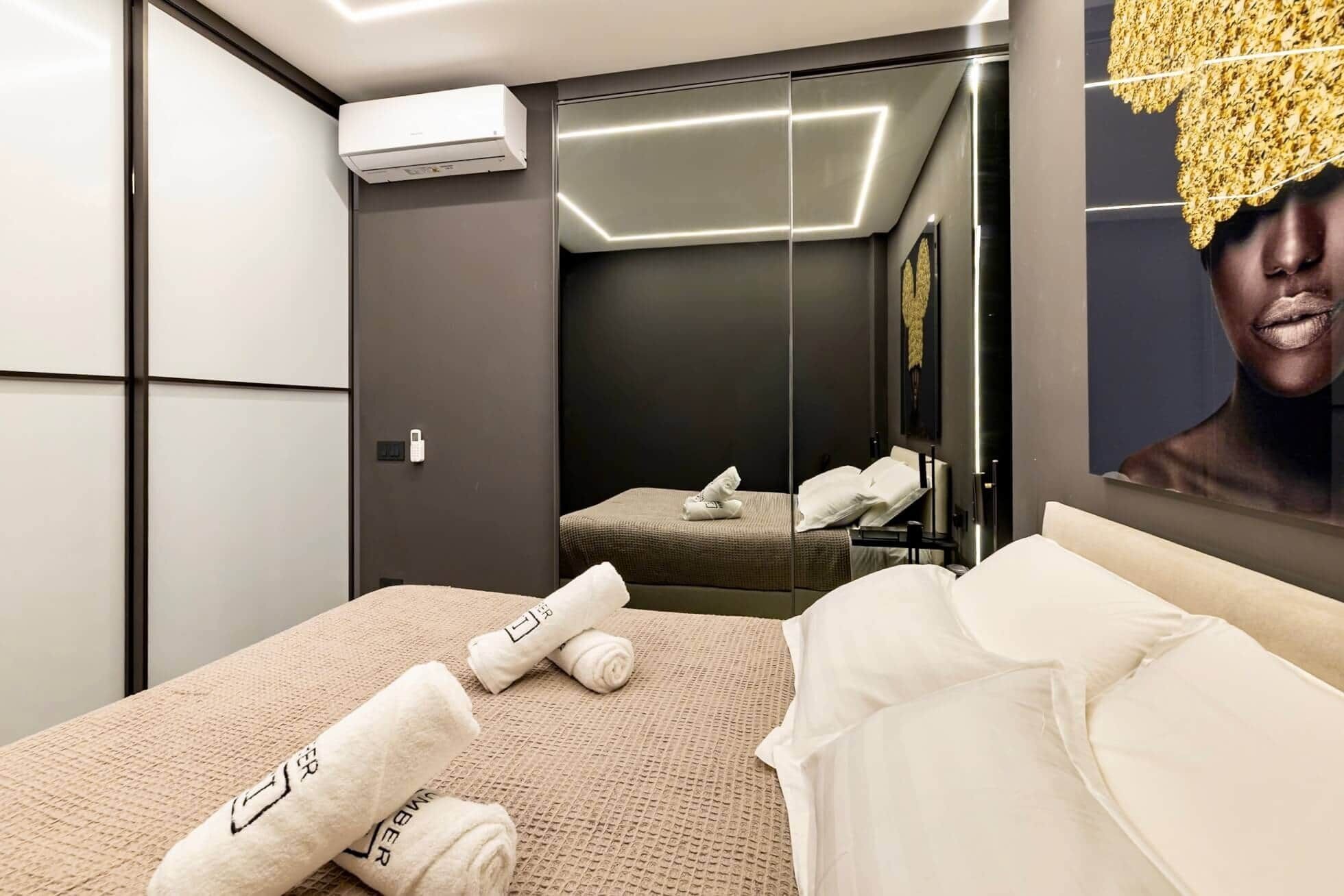 A modern hotel room with a bed, a mirror, and an air conditioning unit.