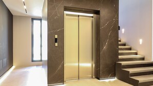 A modern elevator with a marble wall, a light-colored floor, and a staircase with dark steps.