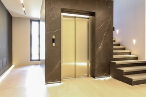 A modern elevator with a marble wall, a light-colored floor, and a staircase with dark steps.