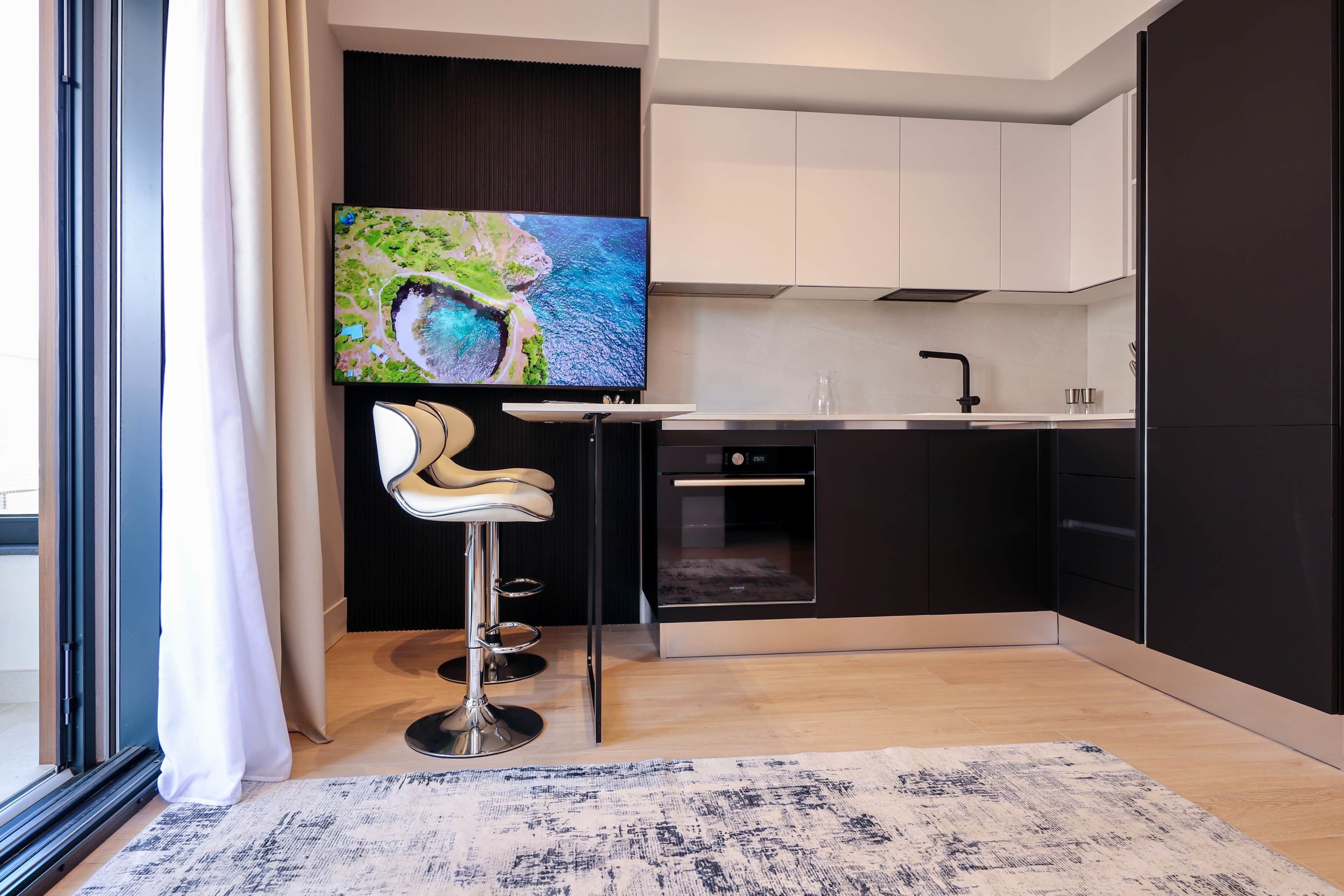 Een moderne keuken met een grote flatscreen-tv, een barkruk en een inbouwoven.