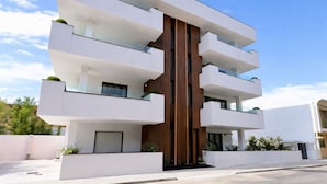 A modern multi-story building with balconies, a central wooden column, and a flat roof.