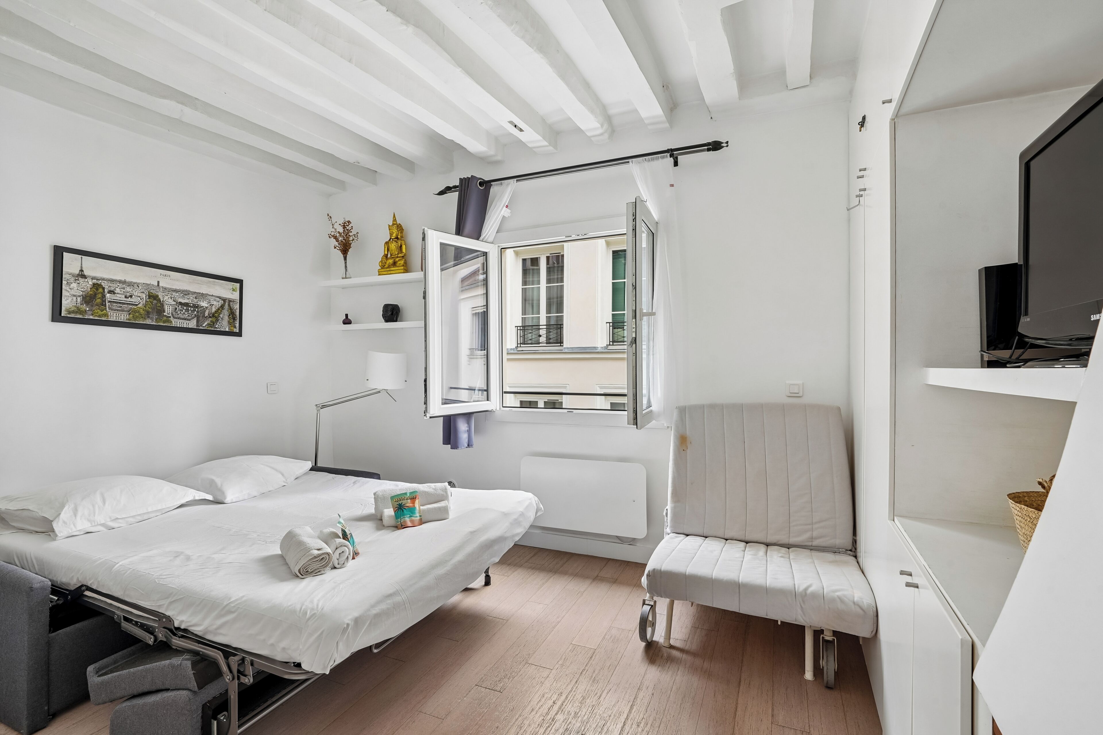 A room with a bed, a chair, a window with curtains, a radiator, and a television.