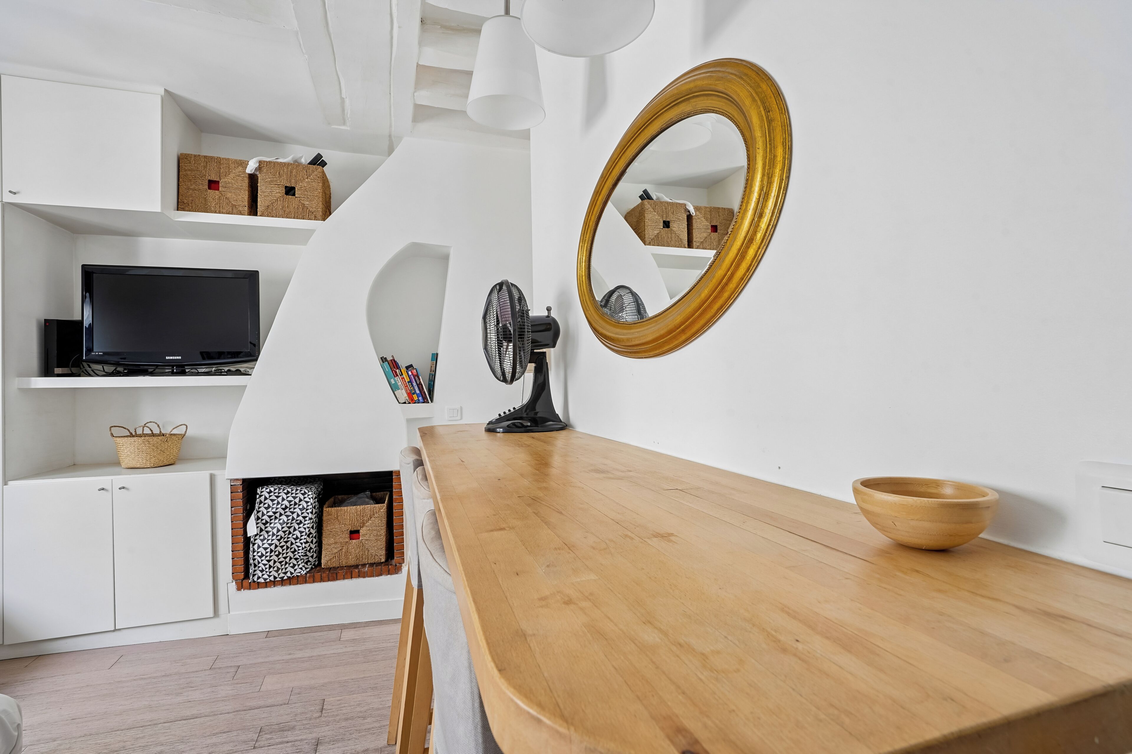 Un salon moderne avec une table à manger en bois, un téléviseur noir et un miroir doté d’un cadre doré.