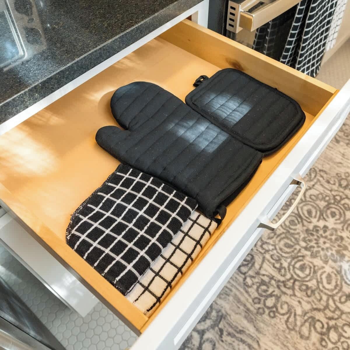 A kitchen drawer with a black and white checkered oven mitt and a black pot holder.
