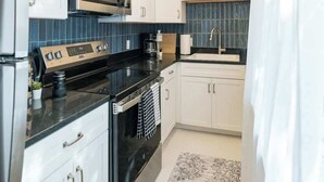 A modern kitchen with white cabinets, a black countertop, a stainless steel refrigerator, a microwave, a coffee maker, and a sink.