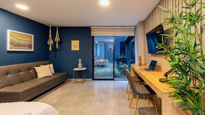 A modern living room with a sofa, a dining table, and a TV. There is a small side table and a plant. - Loft with garden view for natural relaxation (Medellín)