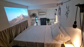 Un dormitorio con cama, ventilador de pared, unidad de aire acondicionado y ventana con vista a la montaña.