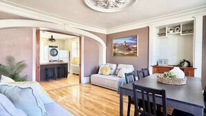 A spacious living room with a sofa, dining table, and kitchen area in the background.