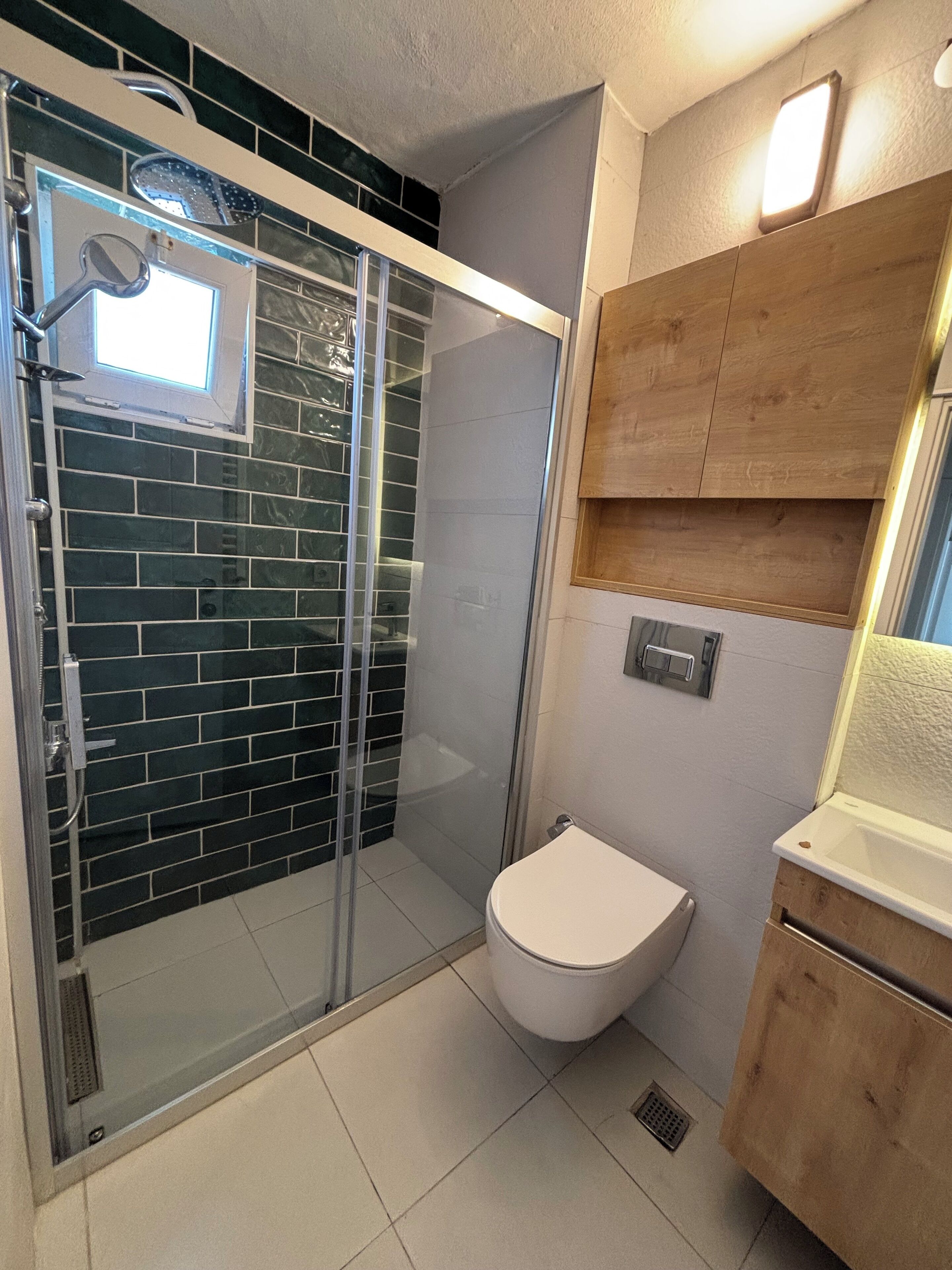 Une salle de bain avec une douche à parois de verre, des toilettes blanches et un meuble-lavabo en bois avec un miroir.