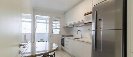 A modern kitchen with white cabinetry, a stainless steel refrigerator, a built-in oven, and a round dining table with chairs.