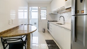 A modern kitchen with white cabinets, a stainless steel refrigerator, a granite countertop, and a dining area with a round table and chairs.