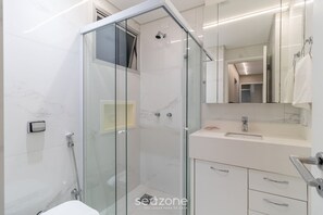 Un baño moderno con ducha envuelta en vidrio, un lavabo blanco y un espejo sobre el mueble.