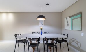 Un comedor moderno con una mesa redonda, sillas negras, un florero azul con flores y una lámpara colgante negra.