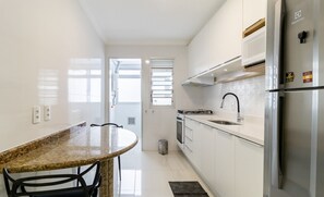 Una cocina moderna con armarios blancos, un refrigerador de acero inoxidable, una encimera de granito y un comedor con una mesa redonda y sillas.
