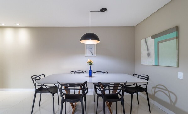 Un comedor moderno con una mesa redonda, sillas negras, un florero azul con flores y una lámpara colgante negra.