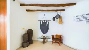A room with a wooden ceiling, a hanging macrame piece, a small table with a vase, and a chair.