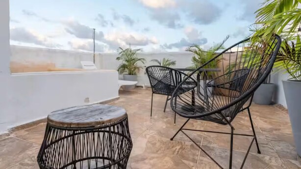 A rooftop terrace with two black wicker chairs, a small round table, and potted plants.