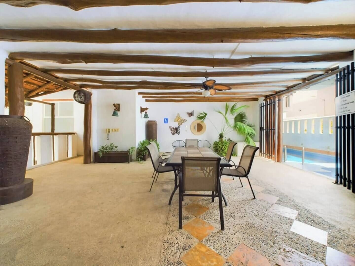 A covered outdoor dining area with a table and chairs, surrounded by plants and decorative items.
