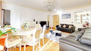 A living room with a dining area, a sofa, a chandelier, and a fireplace.