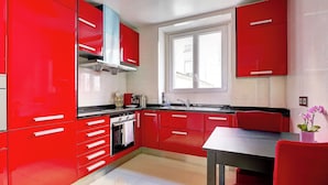 A modern kitchen with red cabinetry, a window, and a dining area.