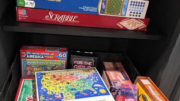 A collection of board games and puzzles on shelves and in a bin.