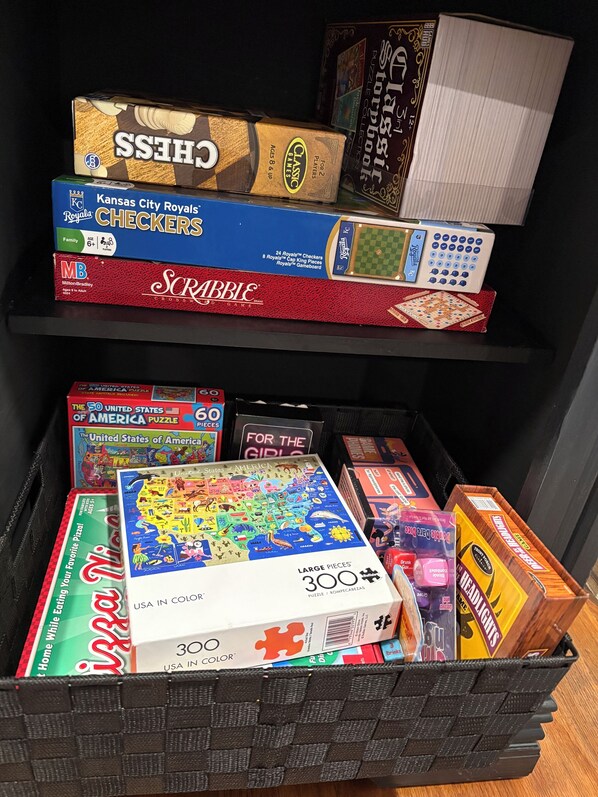 Una colección de juegos de mesa y rompecabezas en estantes y en un cesto.