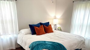Una cama bien tendida con un edredón verde aguamarina, un banco capitonado azul y una alfombra estampada sobre piso de madera.