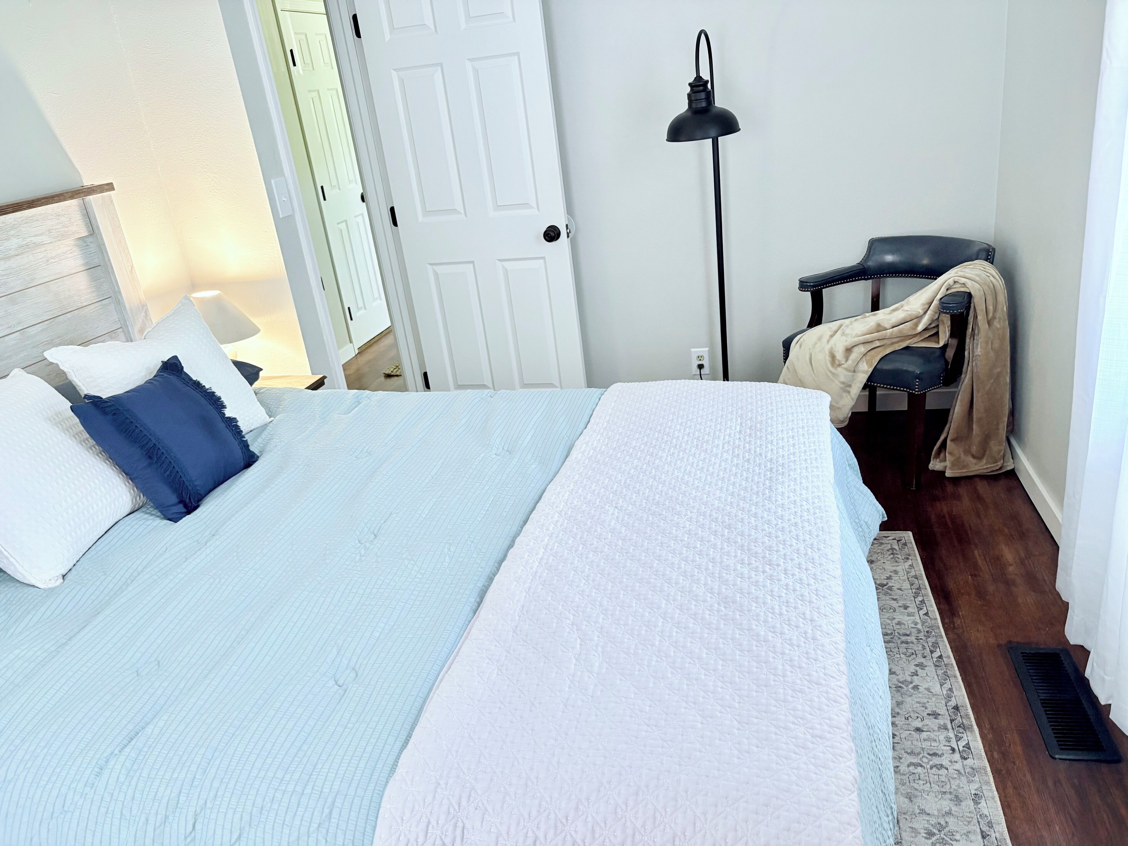 Un dormitorio con cama, lámpara, silla y puerta.